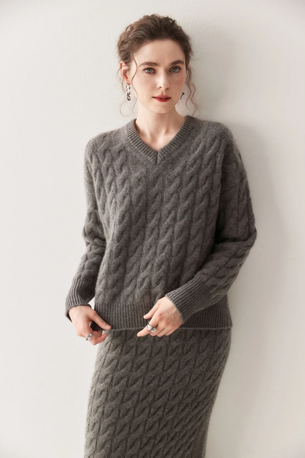 Woman wearing a gray cable knit sweater and skirt against a white background