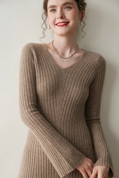 Woman wearing a camel coloured ribbed dress against a plain wall