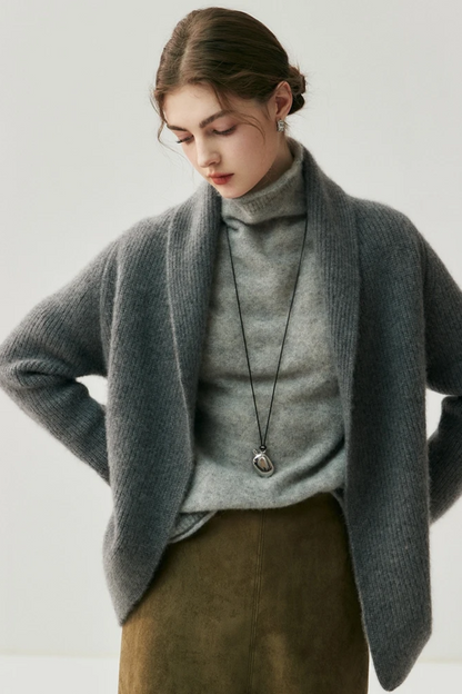 Woman wearing a gray cardigan over a turtleneck sweater with a plain background