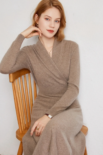 Woman wearing a beige wrap dress sitting on a wooden chair against a white wall.