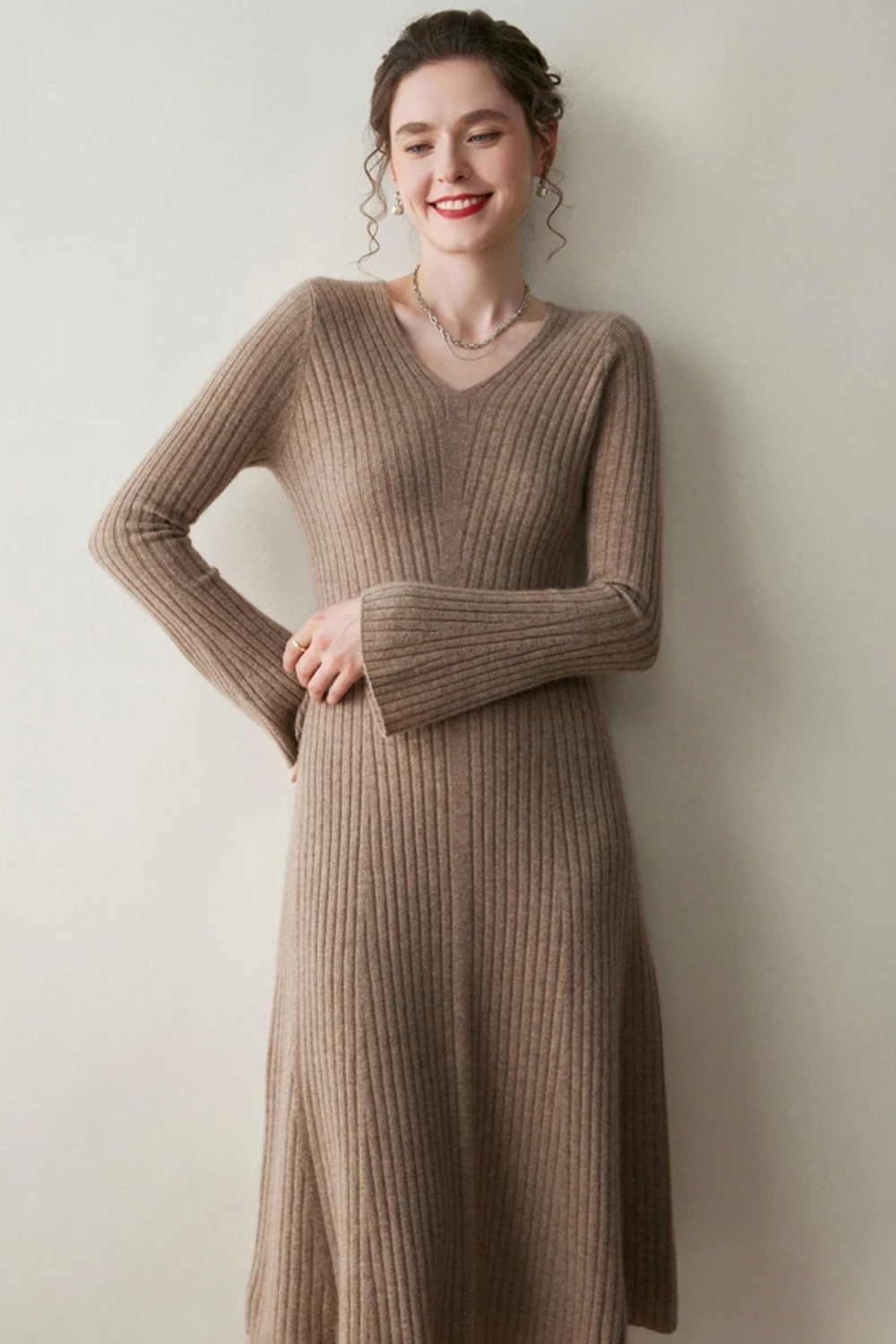 Woman wearing a camel coloured ribbed dress against a plain wall