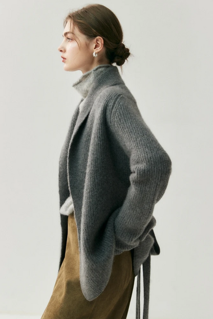 Woman wearing a gray cardigan over a turtleneck sweater facing the side with a plain background