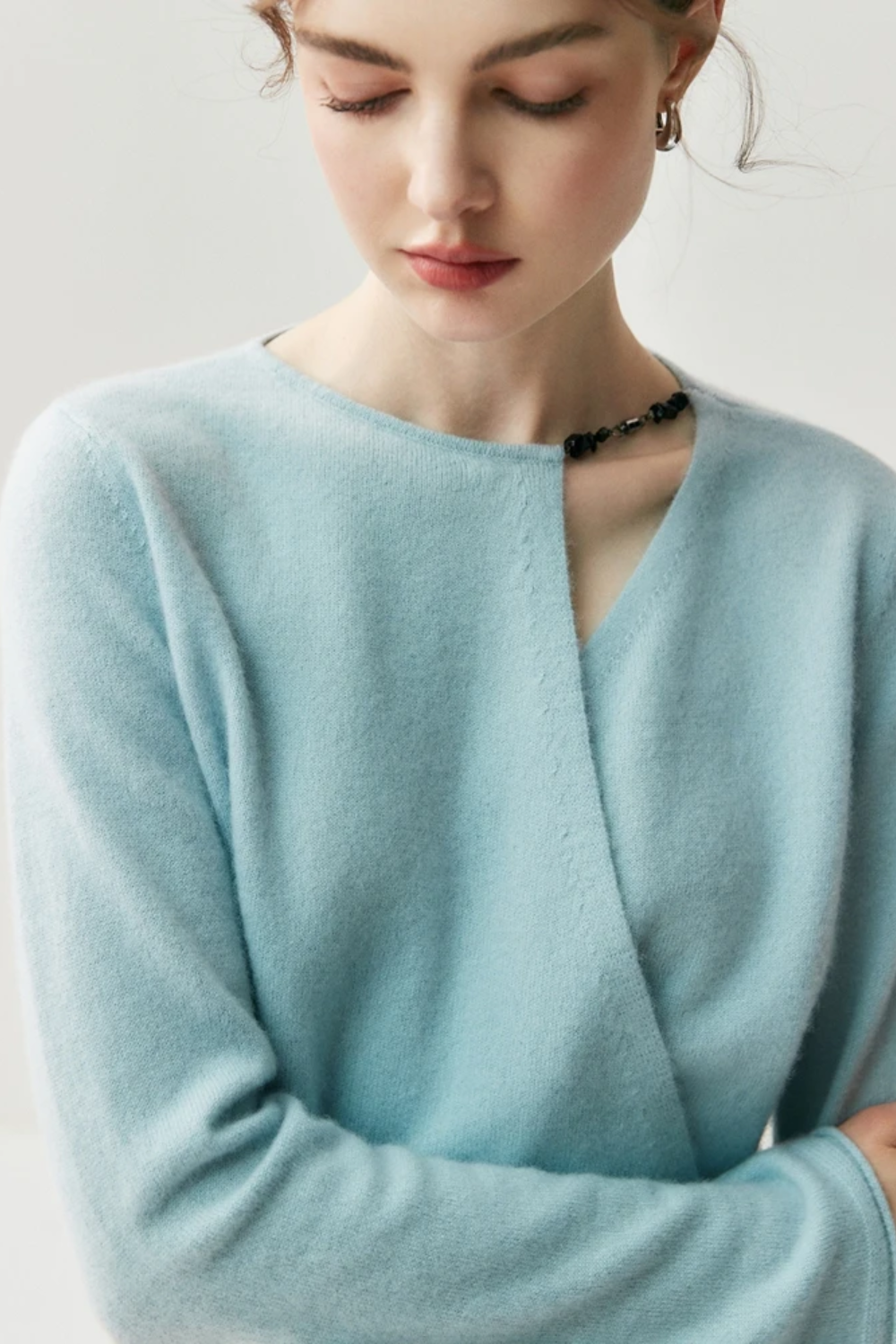 Woman wearing a light blue sweater with a cut out on the shoulder on a plain background