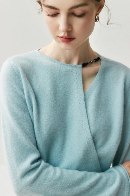 Woman wearing a light blue sweater with a cut out on the shoulder on a plain background