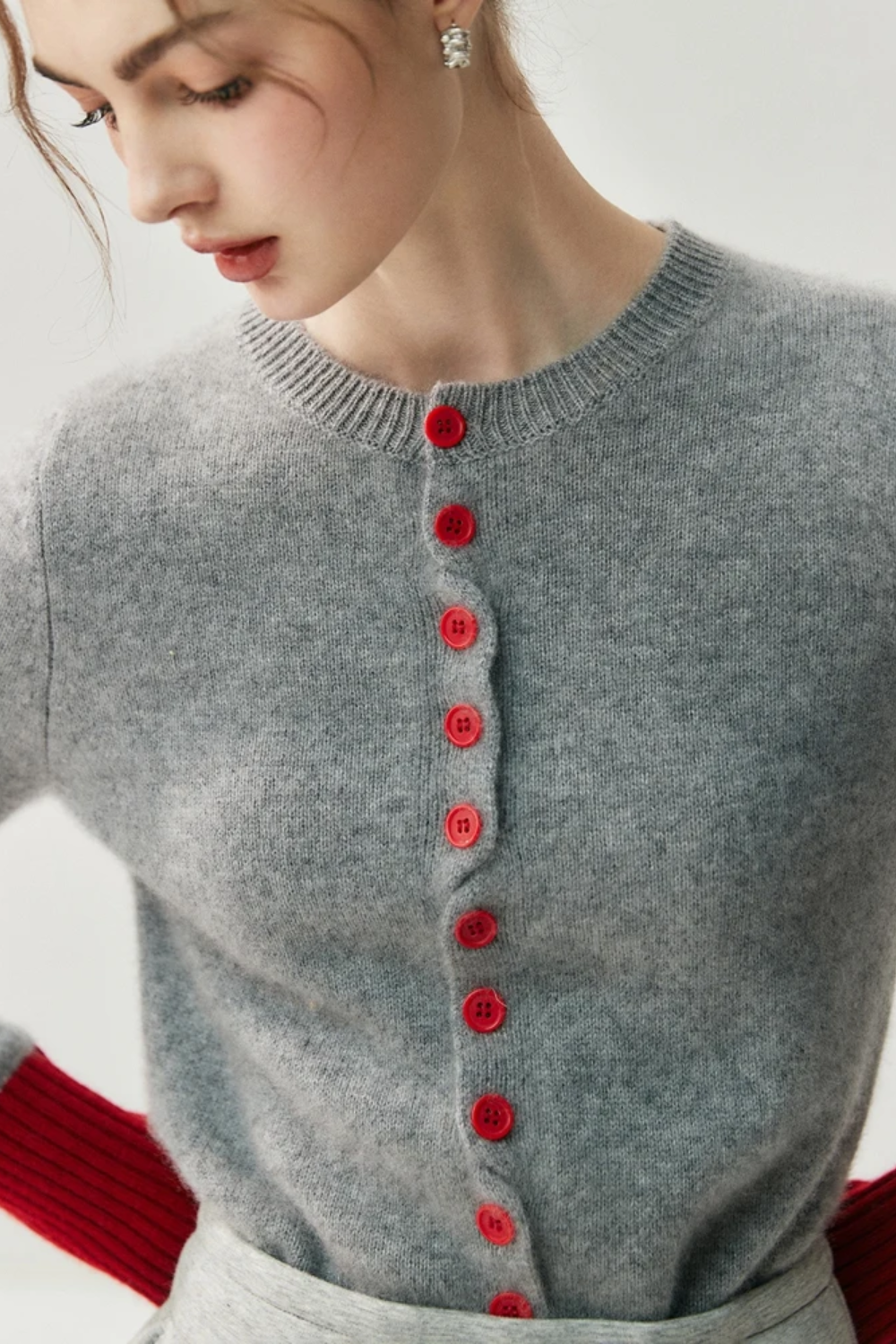 Woman wearing a gray cardigan with red buttons and red sleeves on a light background