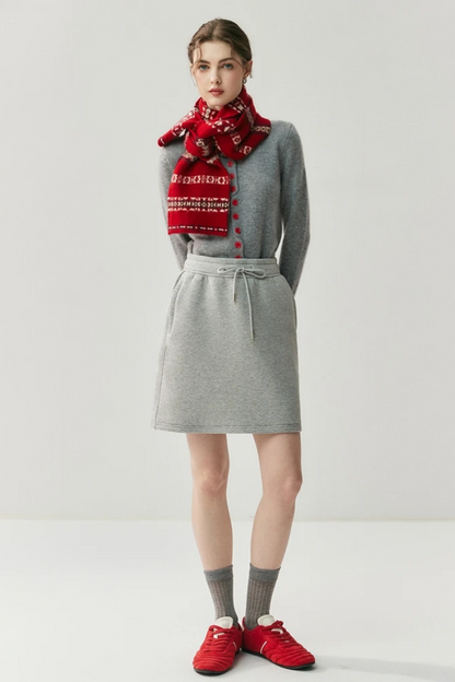 Woman wearing a gray cardigan with red buttons and red sleeves paired with a thick red scarf on a light background