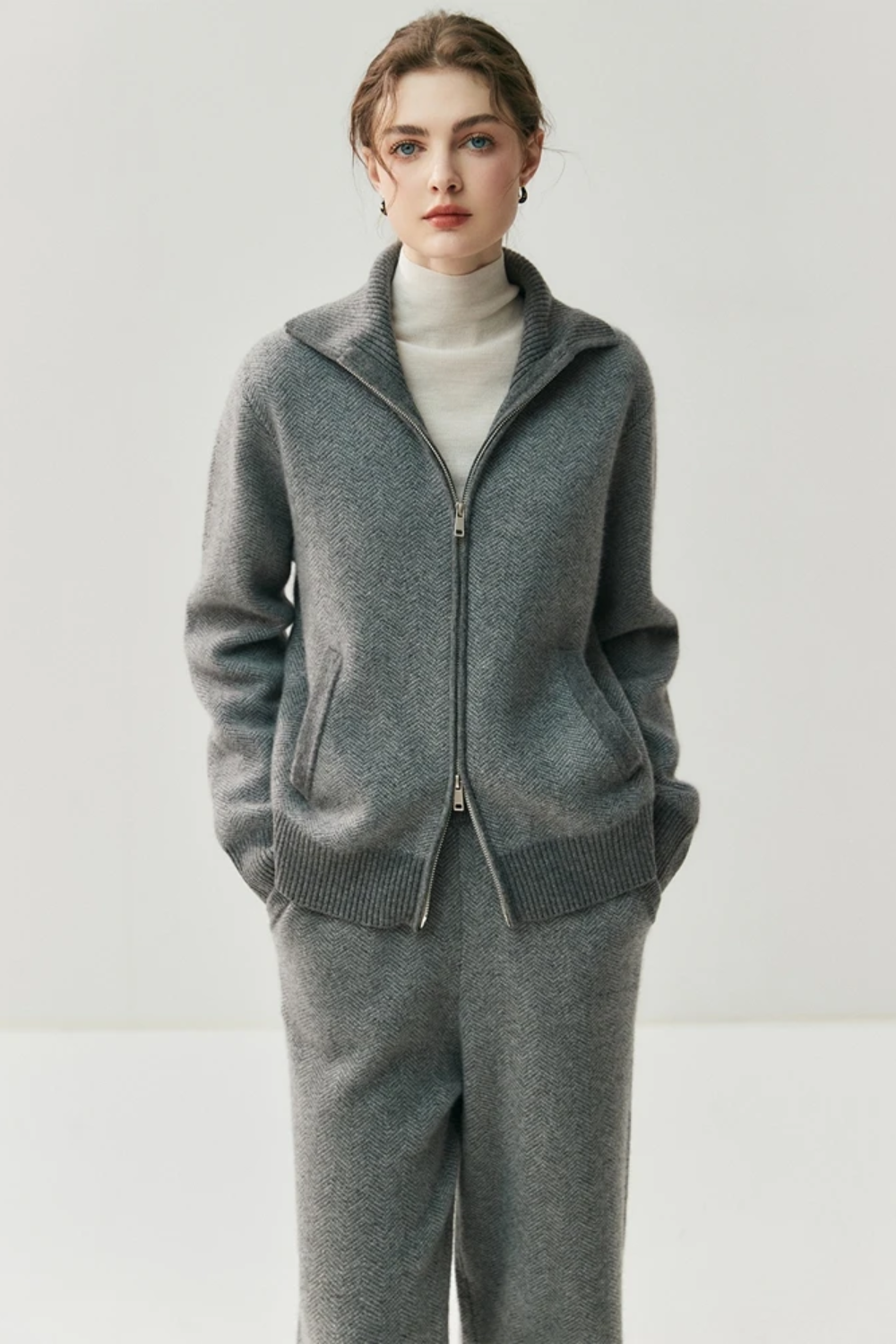 Person wearing a gray zip-up sweater over a white turtleneck on a plain background