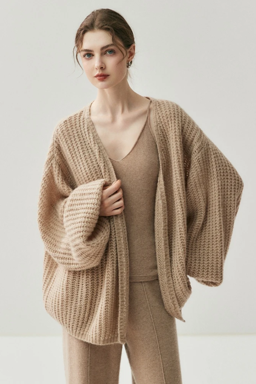 Woman wearing a camel knit cardigan and pants on a white background