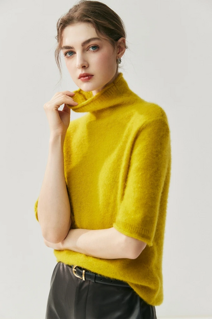 Person wearing a mustard yellow turtleneck sweater with leather pants against a plain background