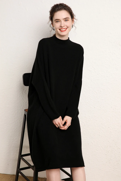 Woman wearing a black dress standing next to a chair against a white wall