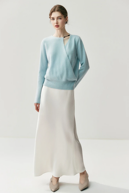 Woman wearing a light blue sweater with a cut out on the shoulder paired with a white skirt on a plain background