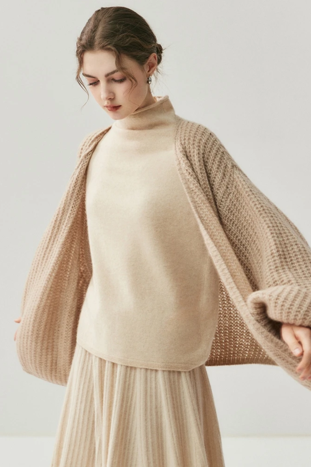 Woman wearing a camel knit cardigan and skirt on a white background