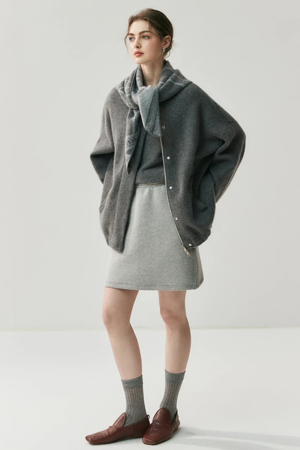 Woman wearing a gray cardigan with a scarf on a white background