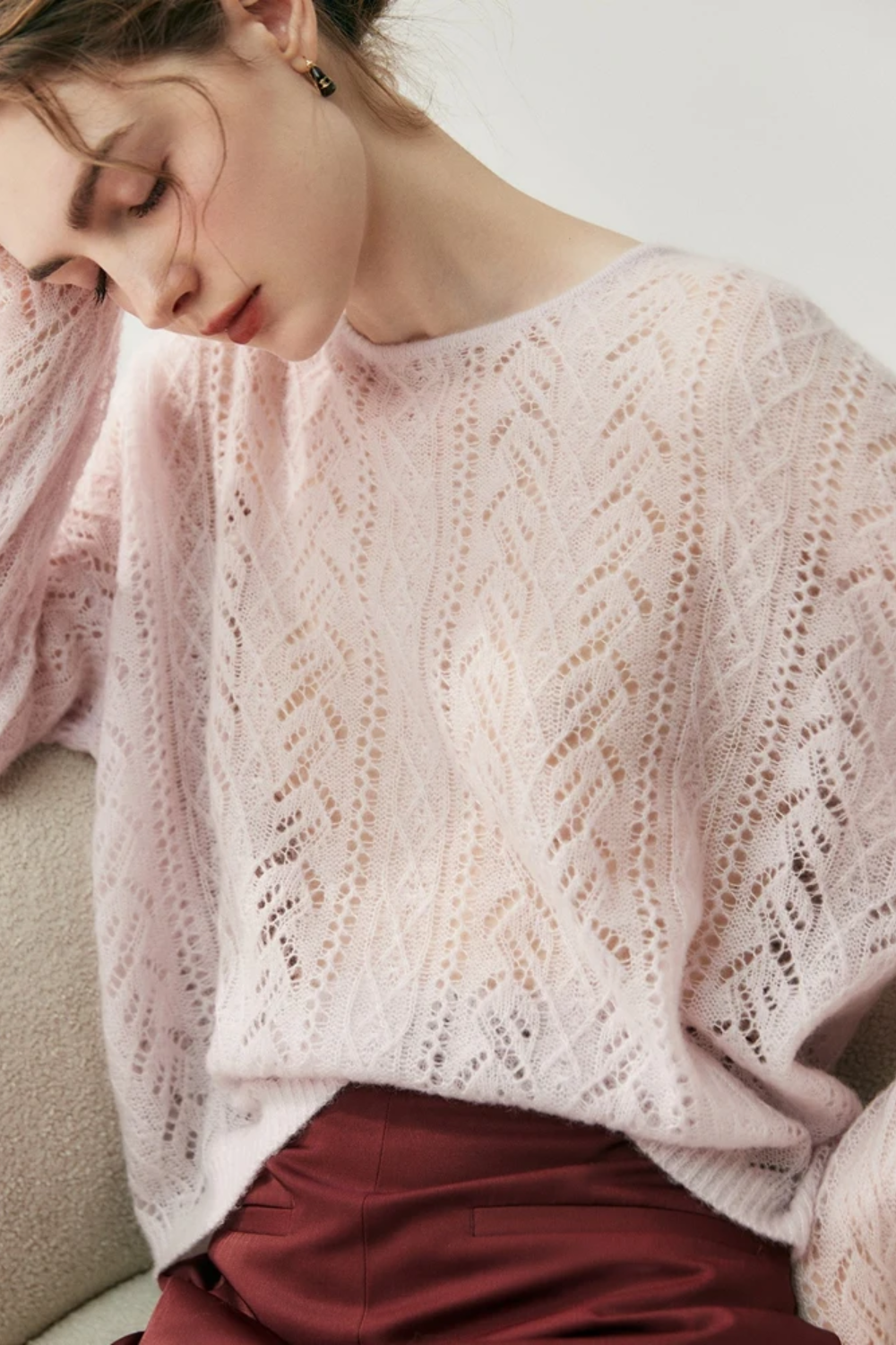 Woman wearing a light pink knitted sweater sitting down on a chair against a white background