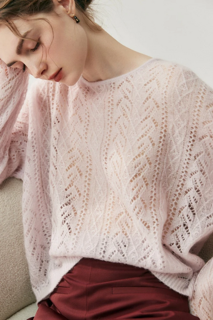 Woman wearing a light pink knitted sweater sitting down on a chair against a white background