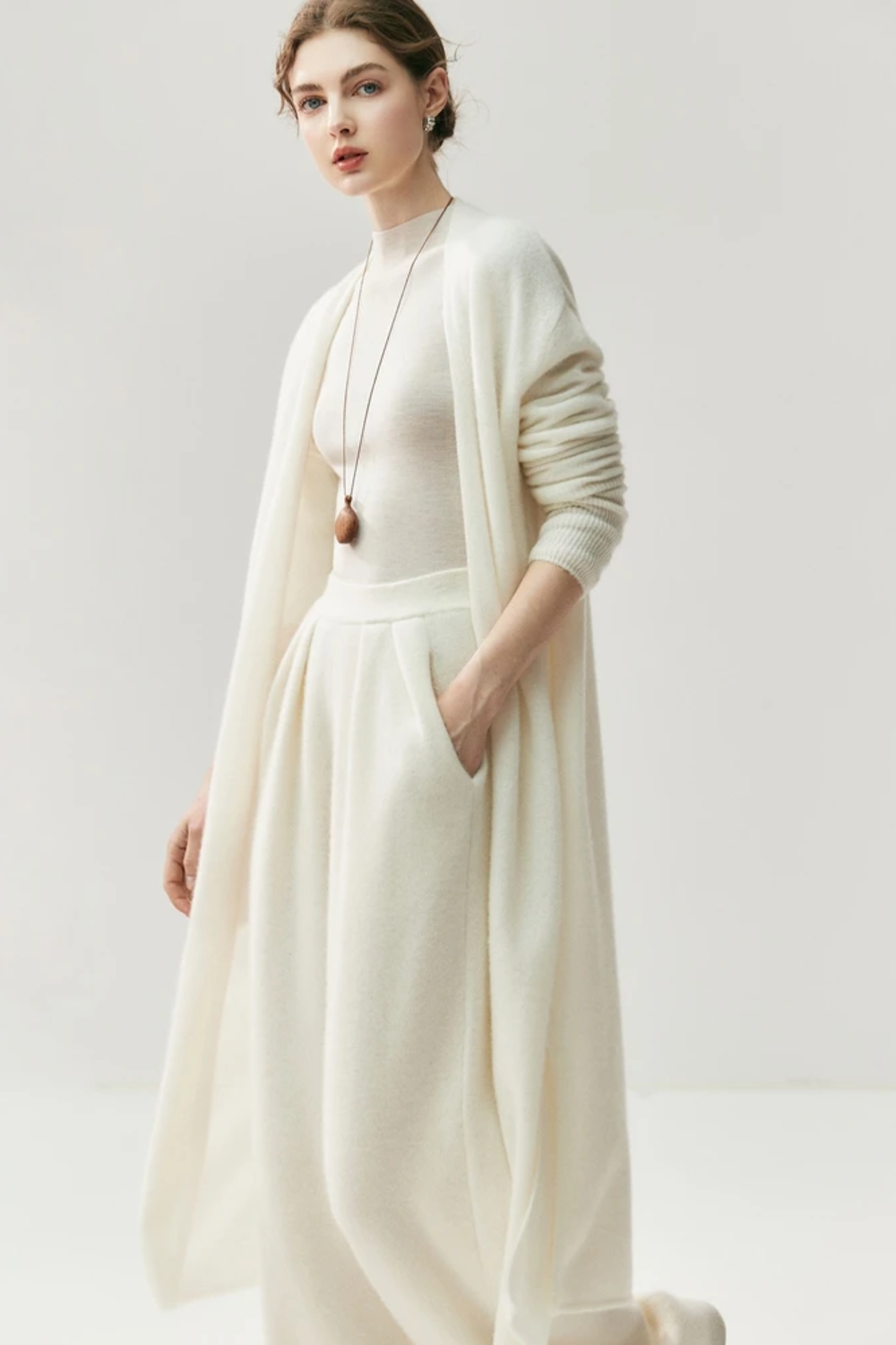 Woman wearing a white outfit with a ahite long cardigan on a white background