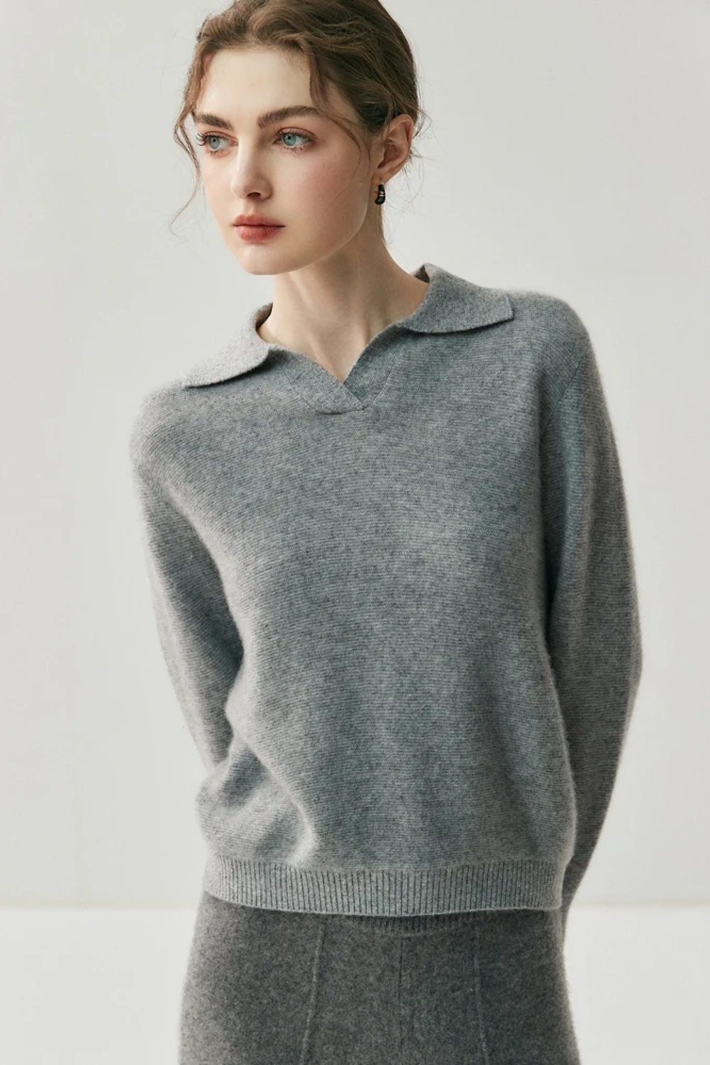 Woman wearing a gray collared sweater and pants against a white background