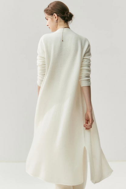 Woman wearing a white outfit with a ahite long cardigan with her back turned on a white background