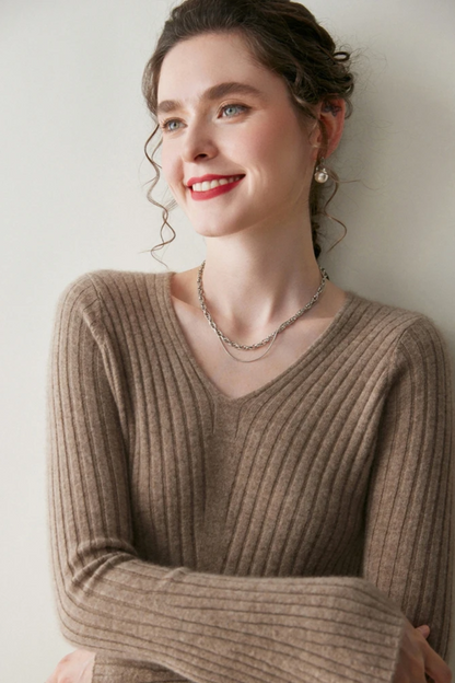 Close up of a woman wearing a camel coloured ribbed dress against a plain wall