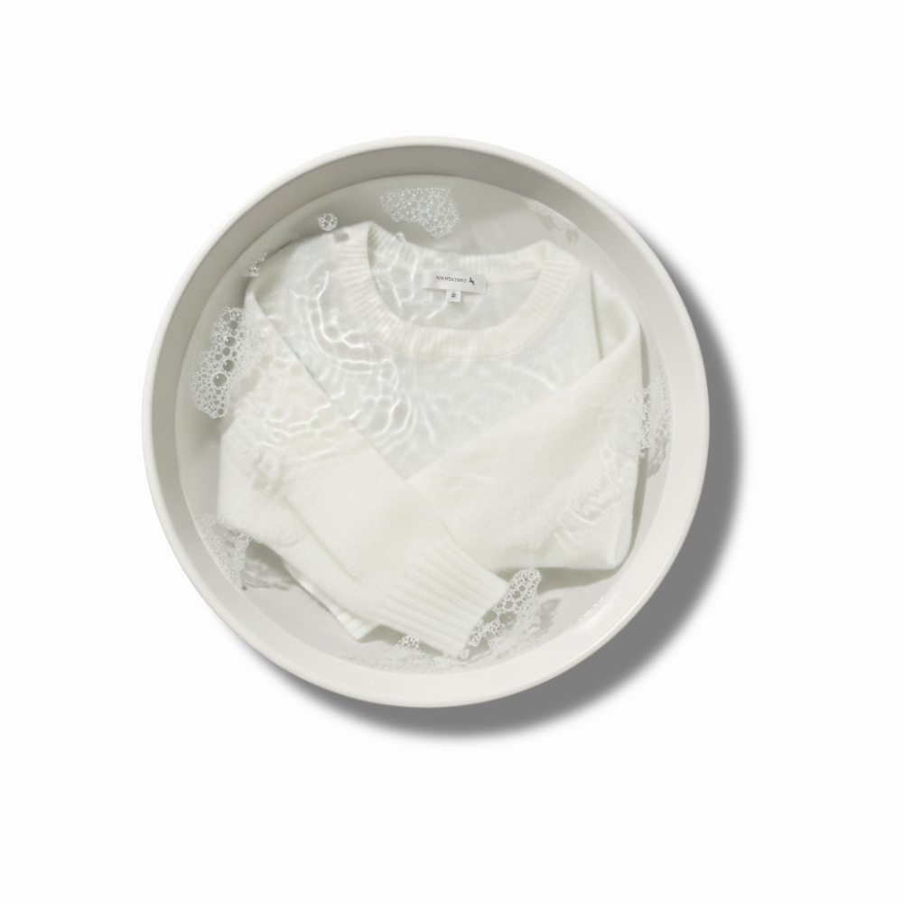 White Cashmere garment in a bowl of water with soap bubbles on a white background