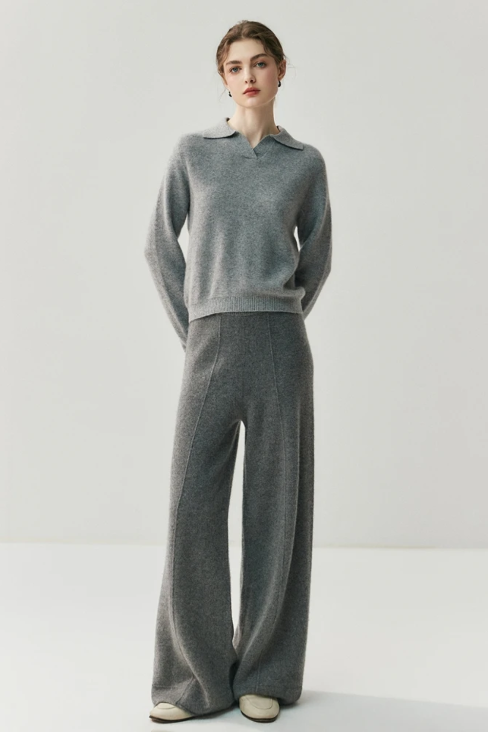 Woman wearing a gray collared sweater and pants against a white background