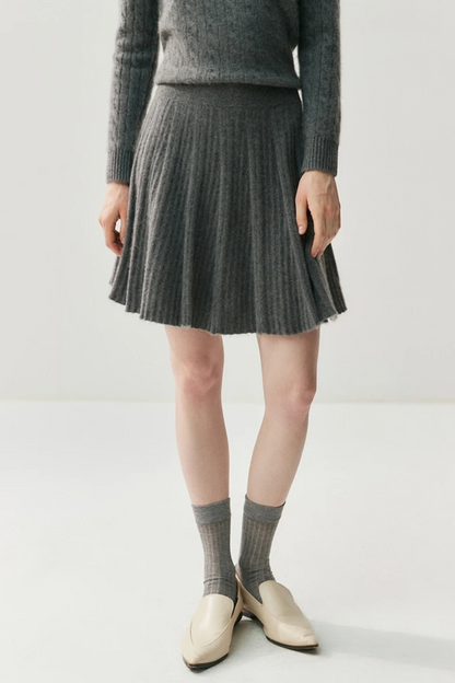Person wearing a gray sweater, pleated skirt, and socks on a white background