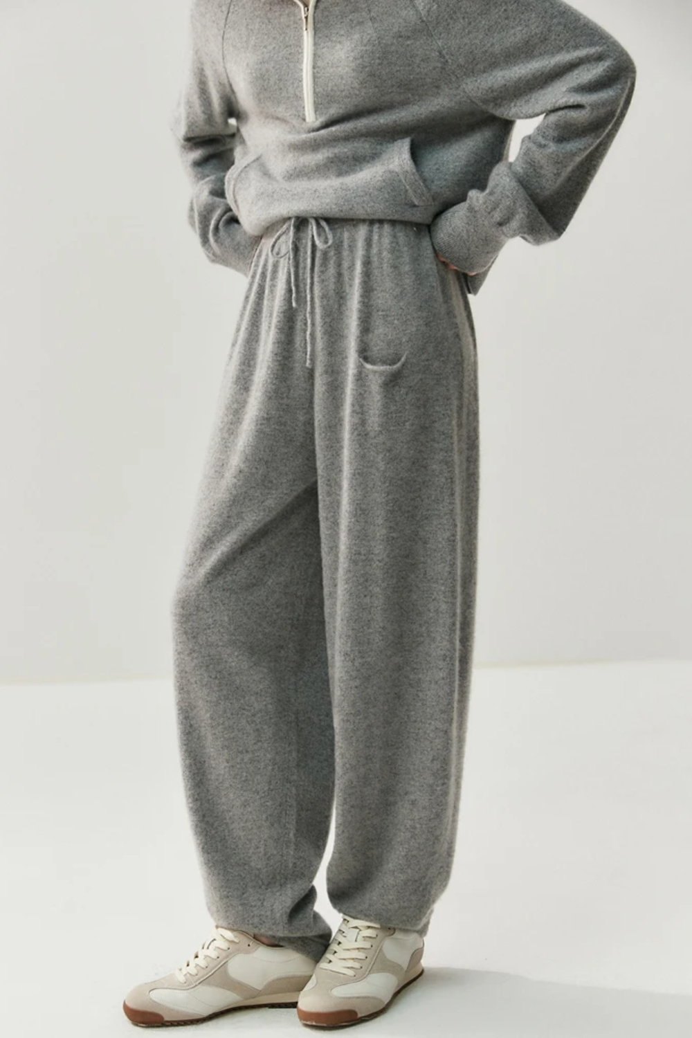 Person wearing a gray tracksuit with white sneakers on a light background