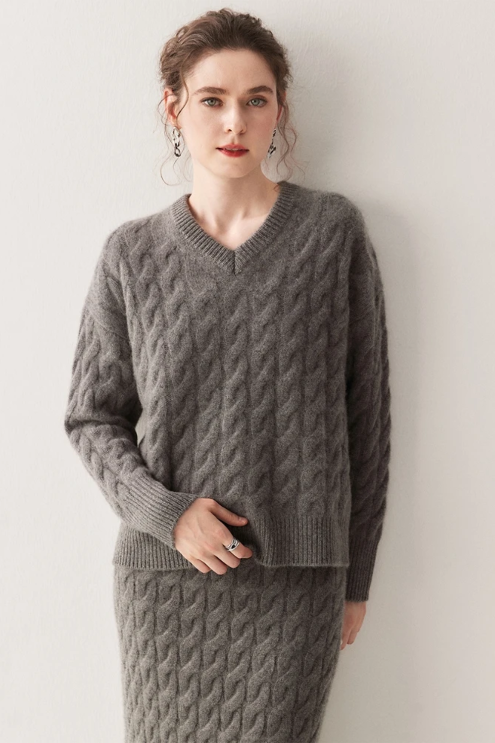 Woman wearing a gray cable knit sweater and skirt against a white background