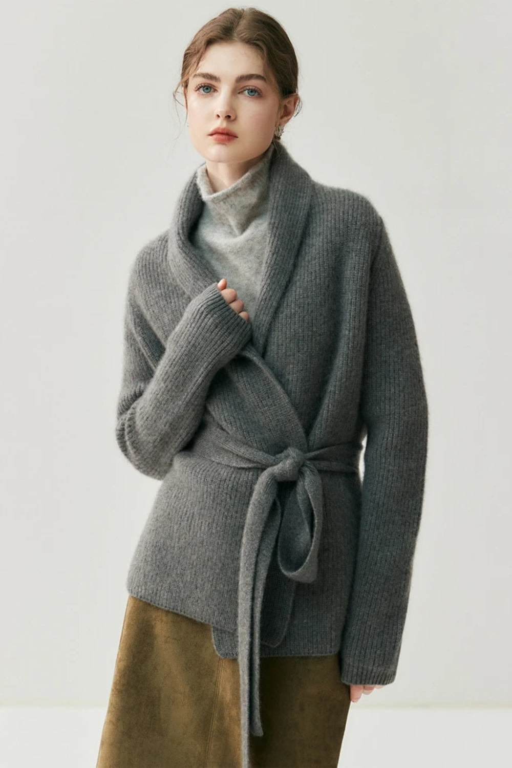 Woman wearing a gray cardigan over a turtleneck sweater with a plain background