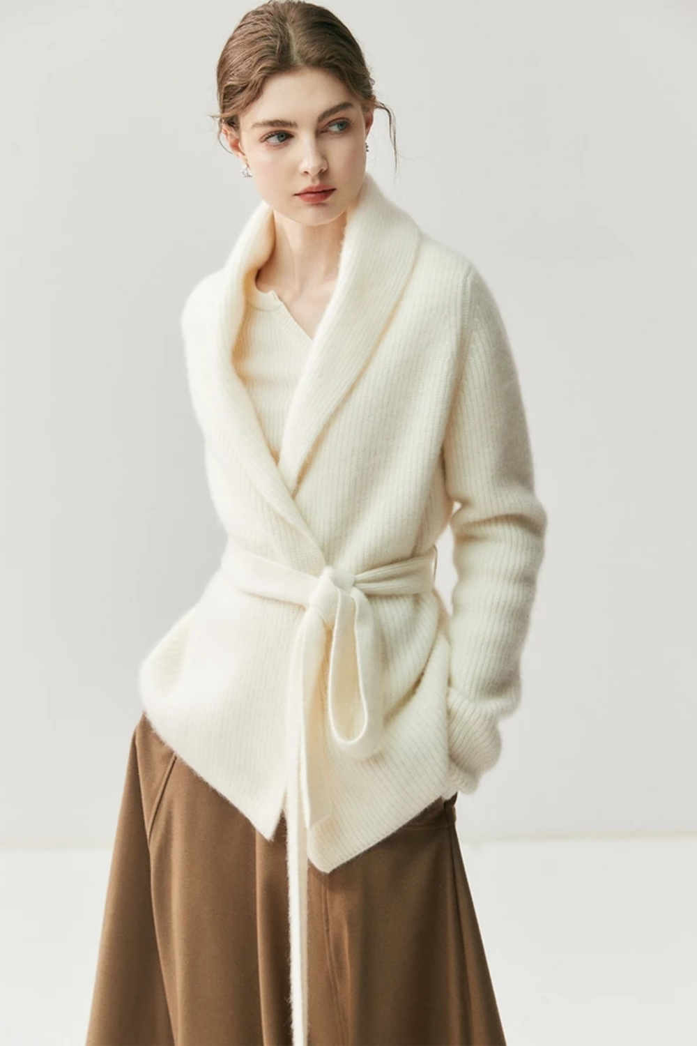 Woman wearing a white cardigan, beige blouse, brown skirt, and beige shoes on a white background