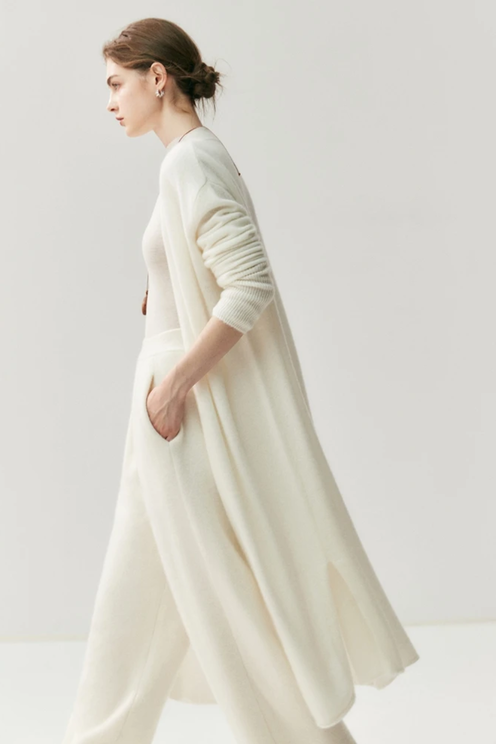 Woman wearing a long,white cardigan against a plain background