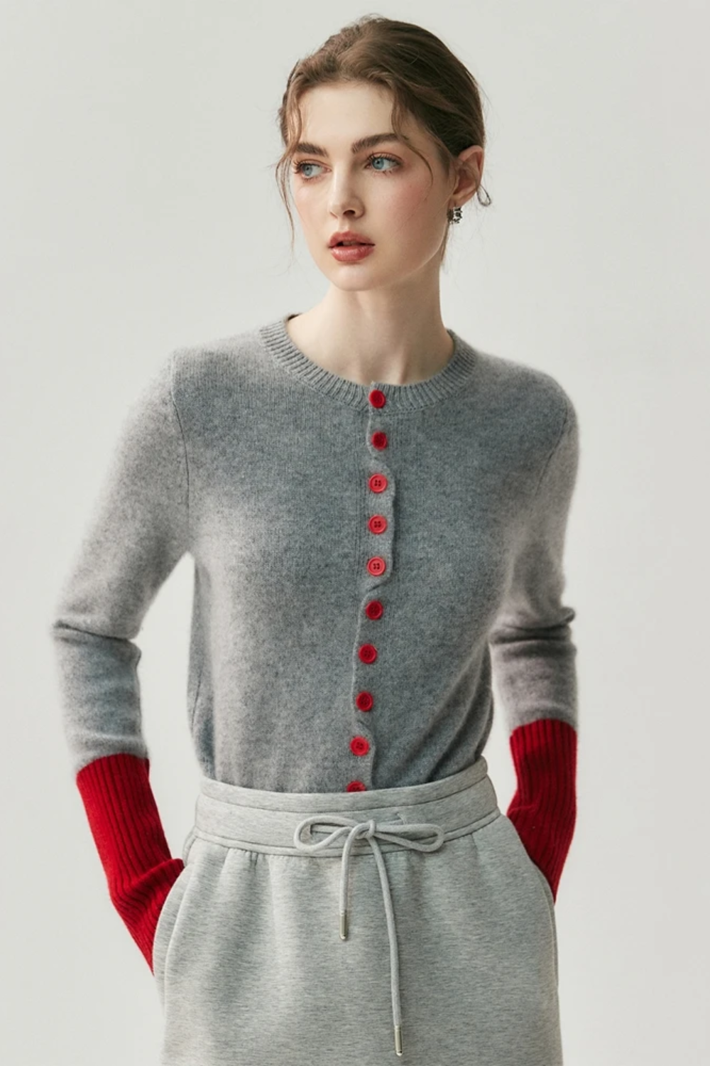 Woman wearing a gray cardigan with red buttons and red sleeves on a light background