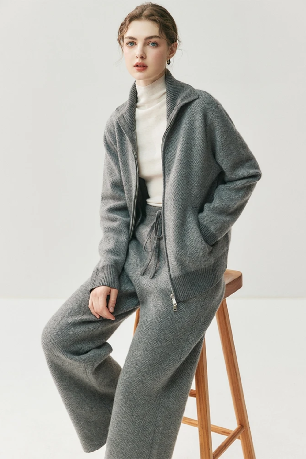 Person wearing a gray tracksuit sitting on a wooden stool against a white background