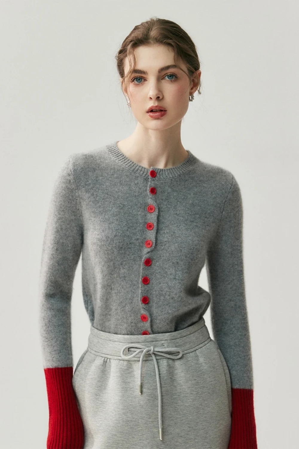 Woman wearing a gray cardigan with red buttons and red sleeves on a light background