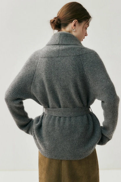 Woman wearing a gray cardigan over a turtleneck sweater turned away with a plain background