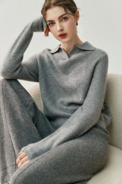 Woman wearing a gray collared sweater and pants sitting on a chair against a white background
