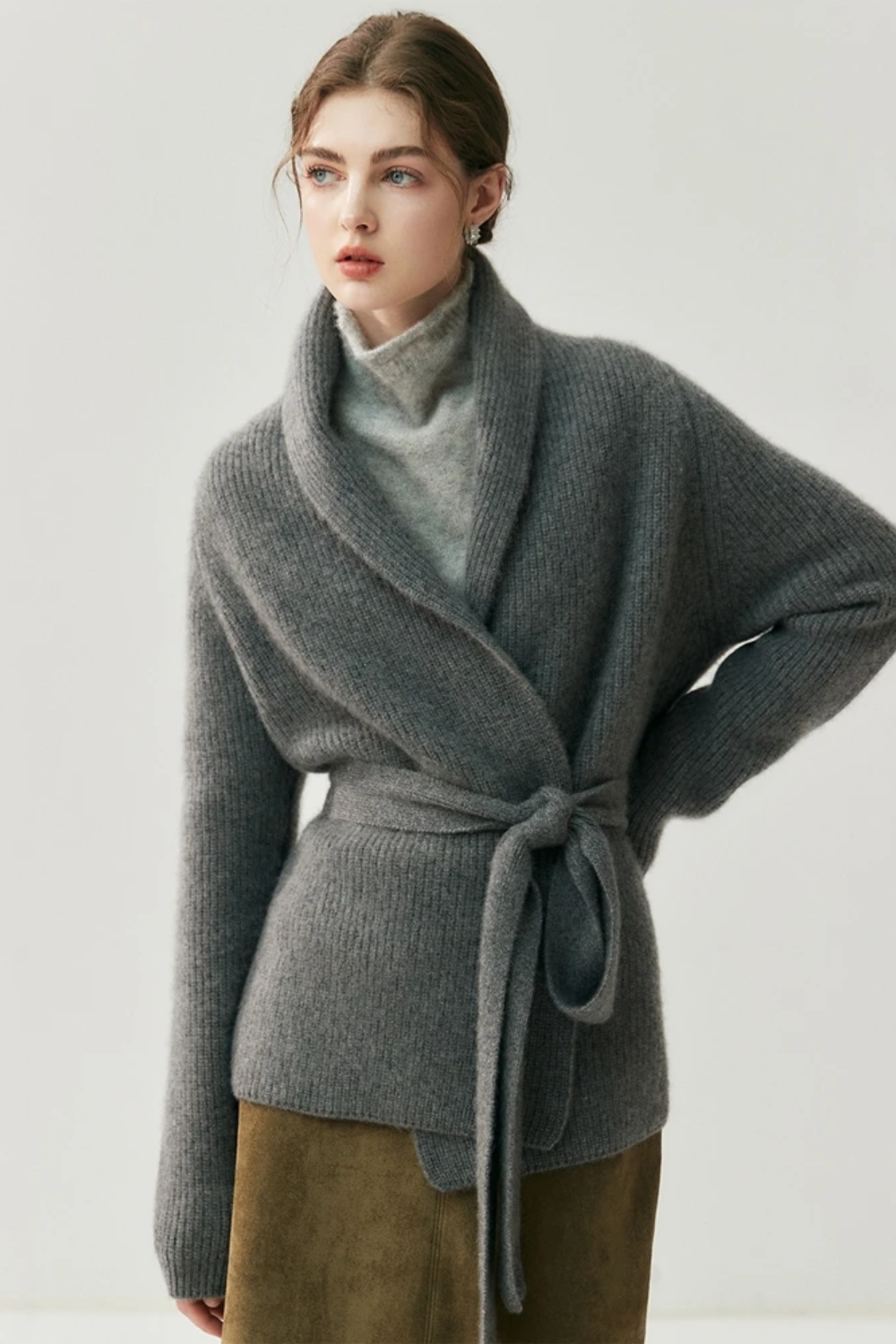 Woman wearing a gray cardigan over a turtleneck sweater with a plain background