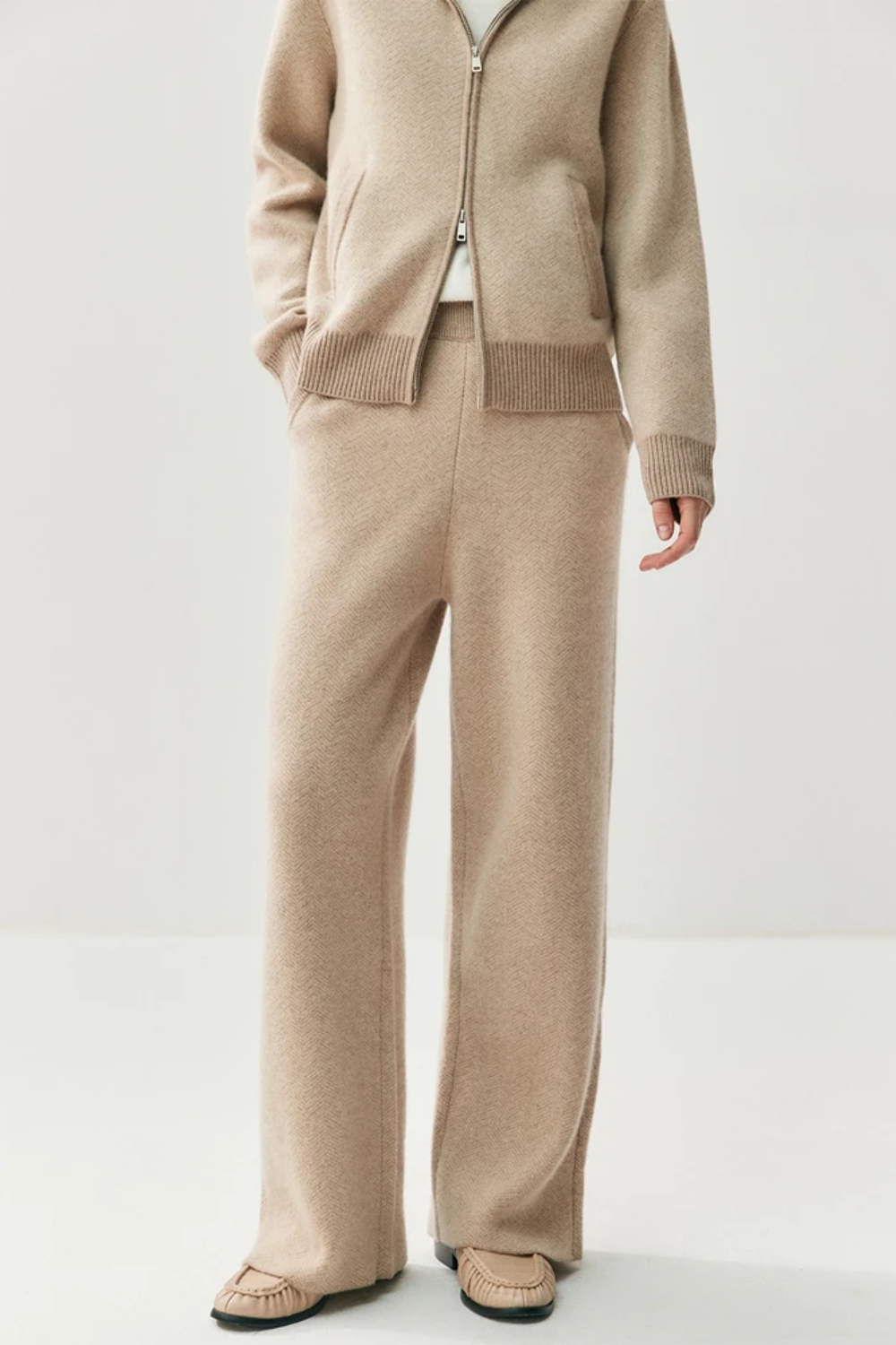 Person wearing a beige sweater and pants on a white background