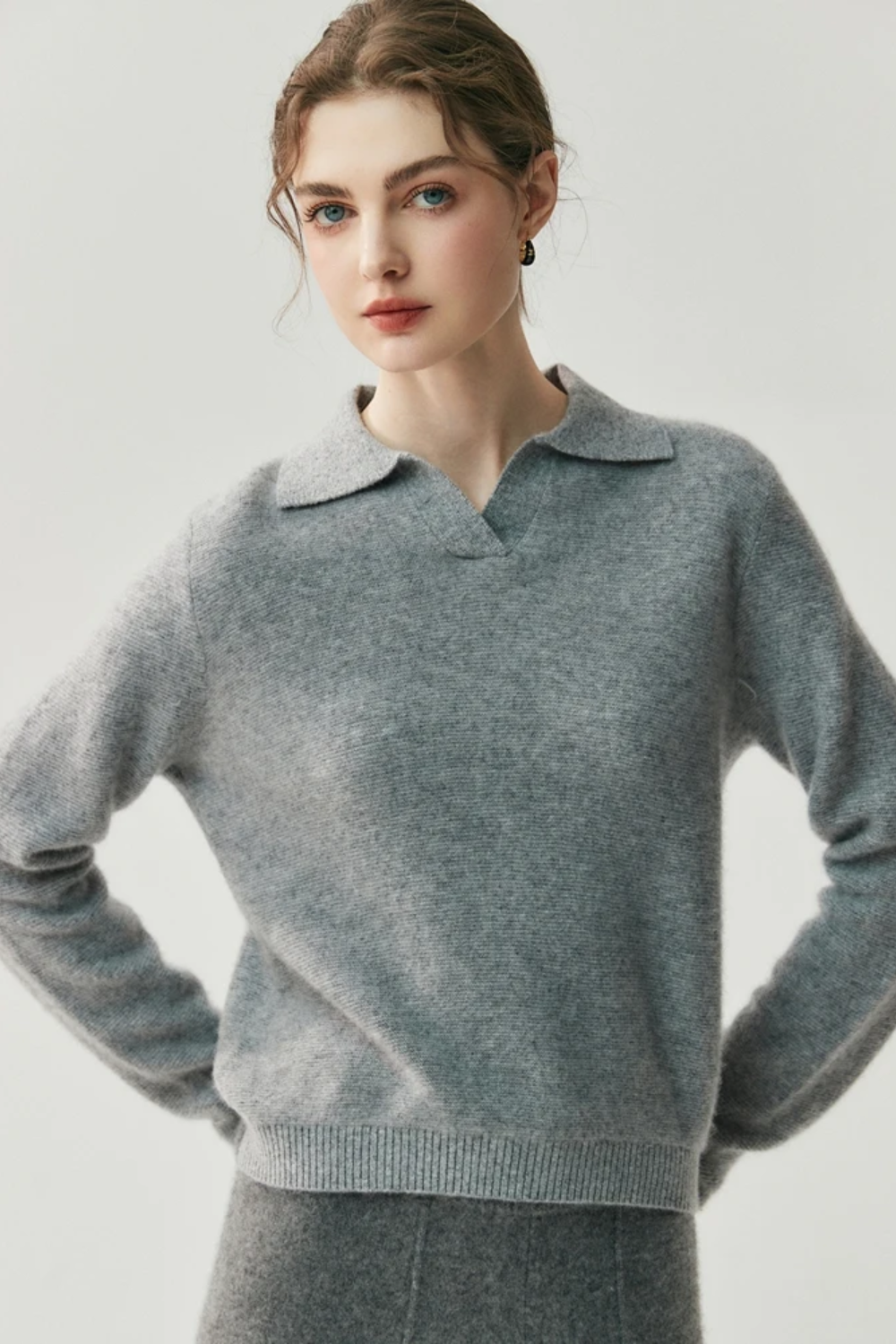 Woman wearing a gray collared sweater and pants against a white background