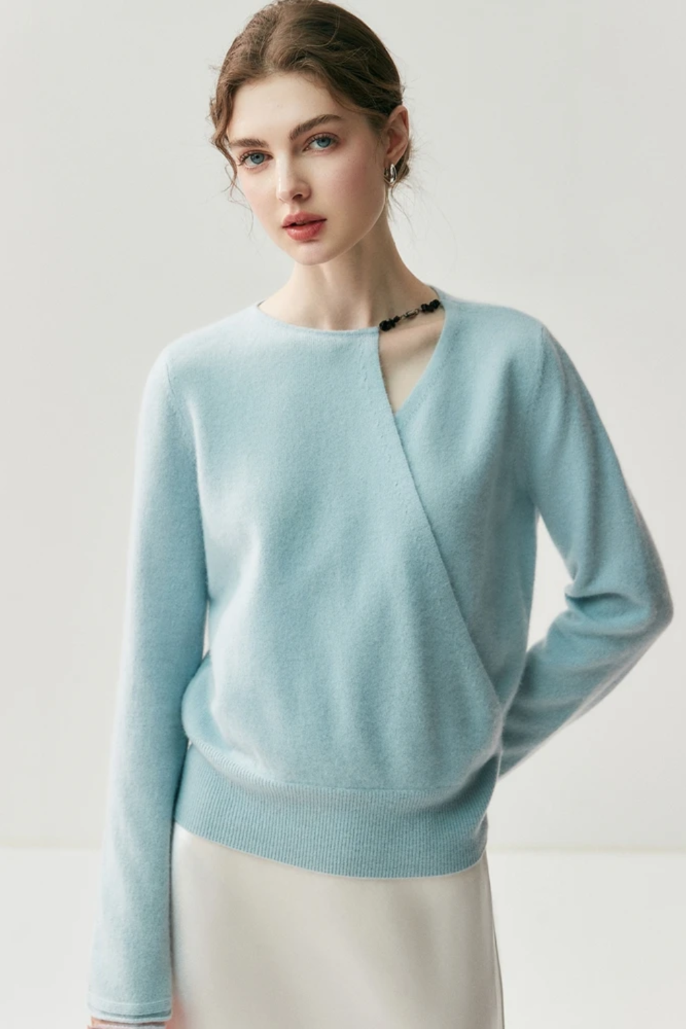 Woman wearing a light blue sweater with a cut out on the shoulder on a plain background