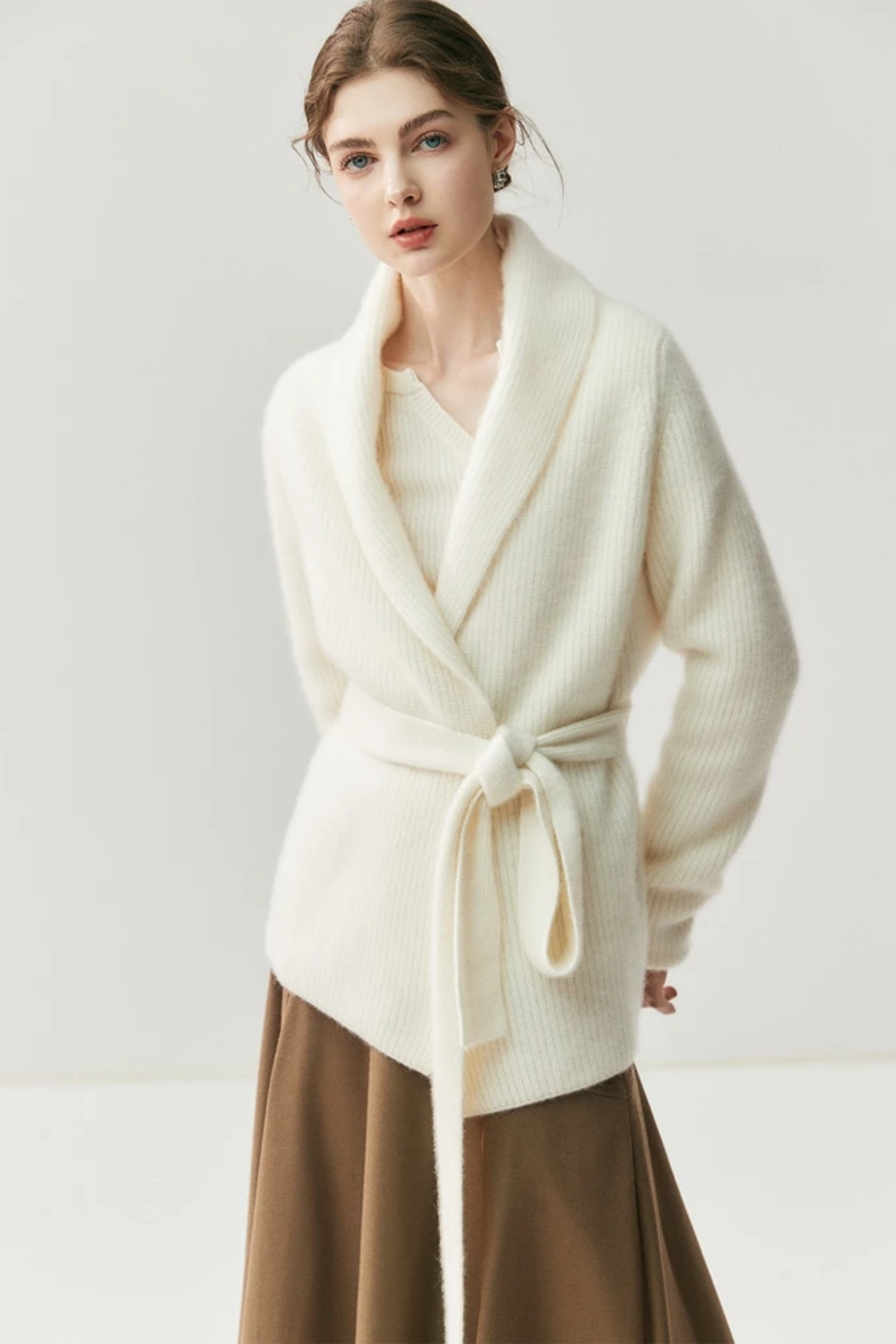 Woman wearing a white cardigan, beige blouse, brown skirt, and beige shoes on a white background