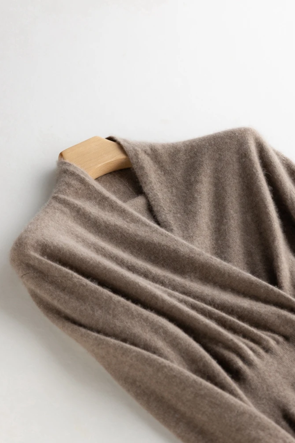 Beige wrap dress draped over a wooden hanger on a white background