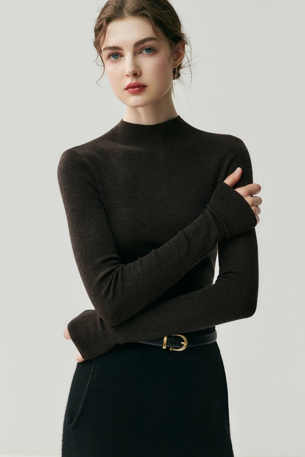 Woman wearing a dark brown turtleneck sweater against a plain background
