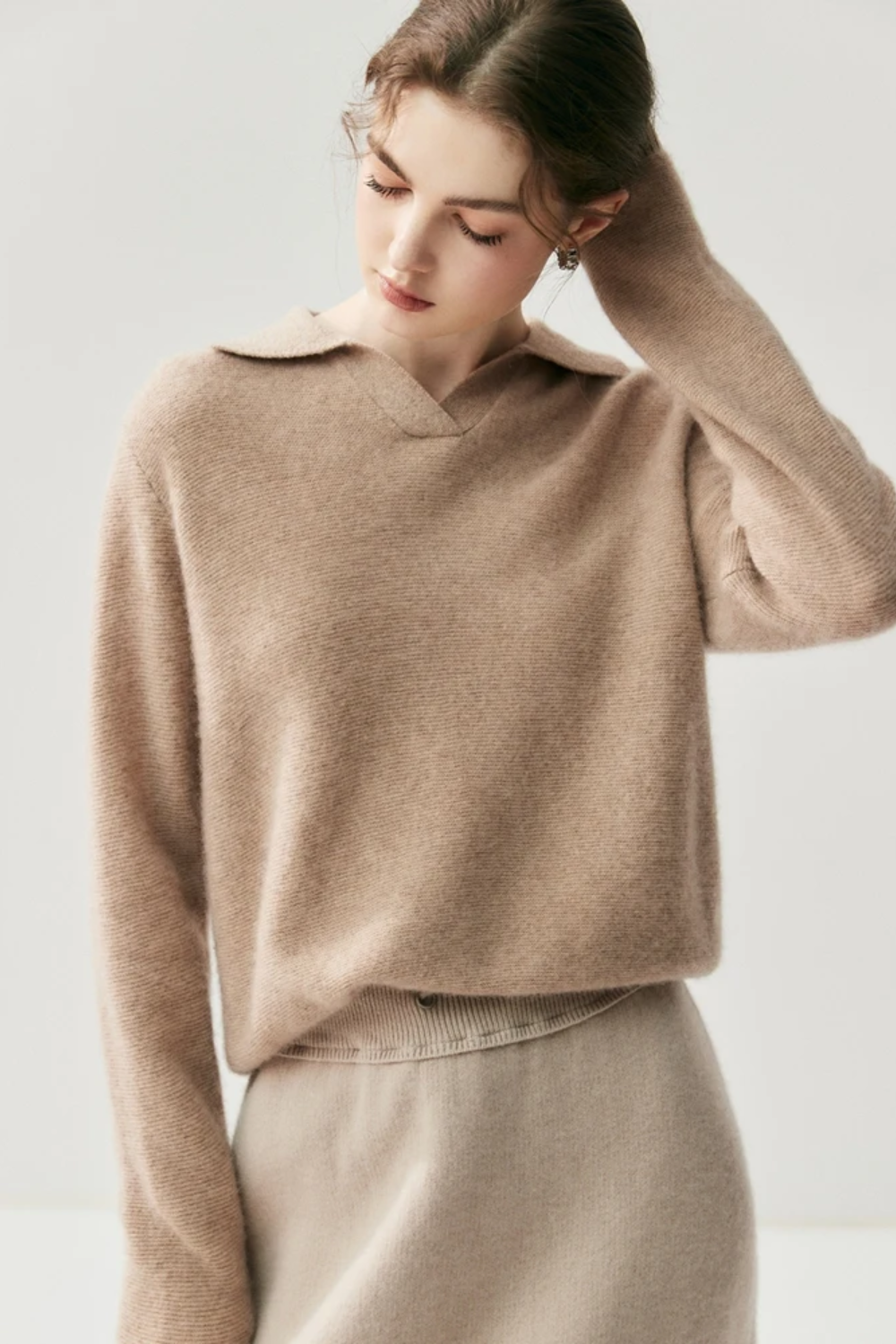 Woman wearing a camel coloured sweater against a plain background