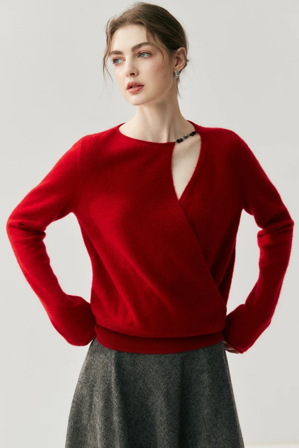 Woman wearing a red sweater with a cut out on the shoulder on a plain background