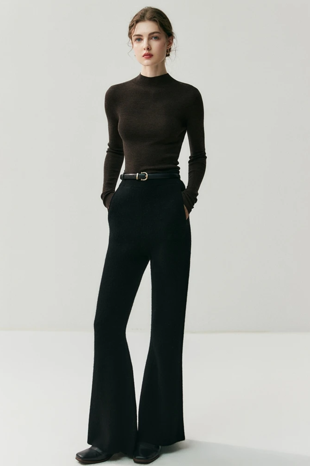 Person wearing a dark brown turtleneck and black bell-bottom pants on a white background