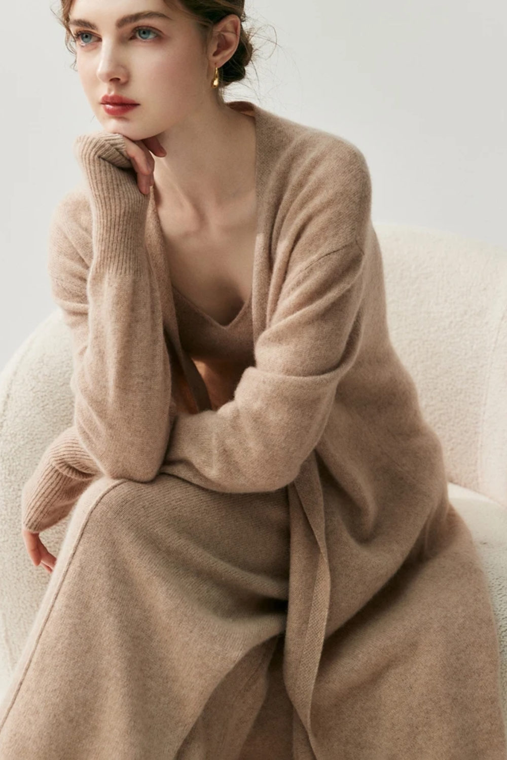Woman wearing a camel sweater and pants set sitting down on a chair