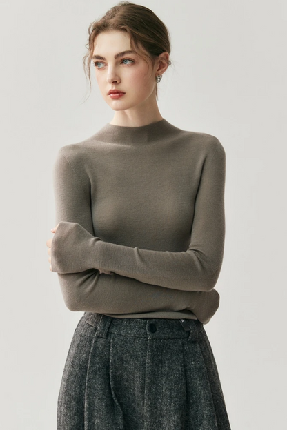 Woman wearing a brown taupe sweater and gray pleated pants on a light gray background