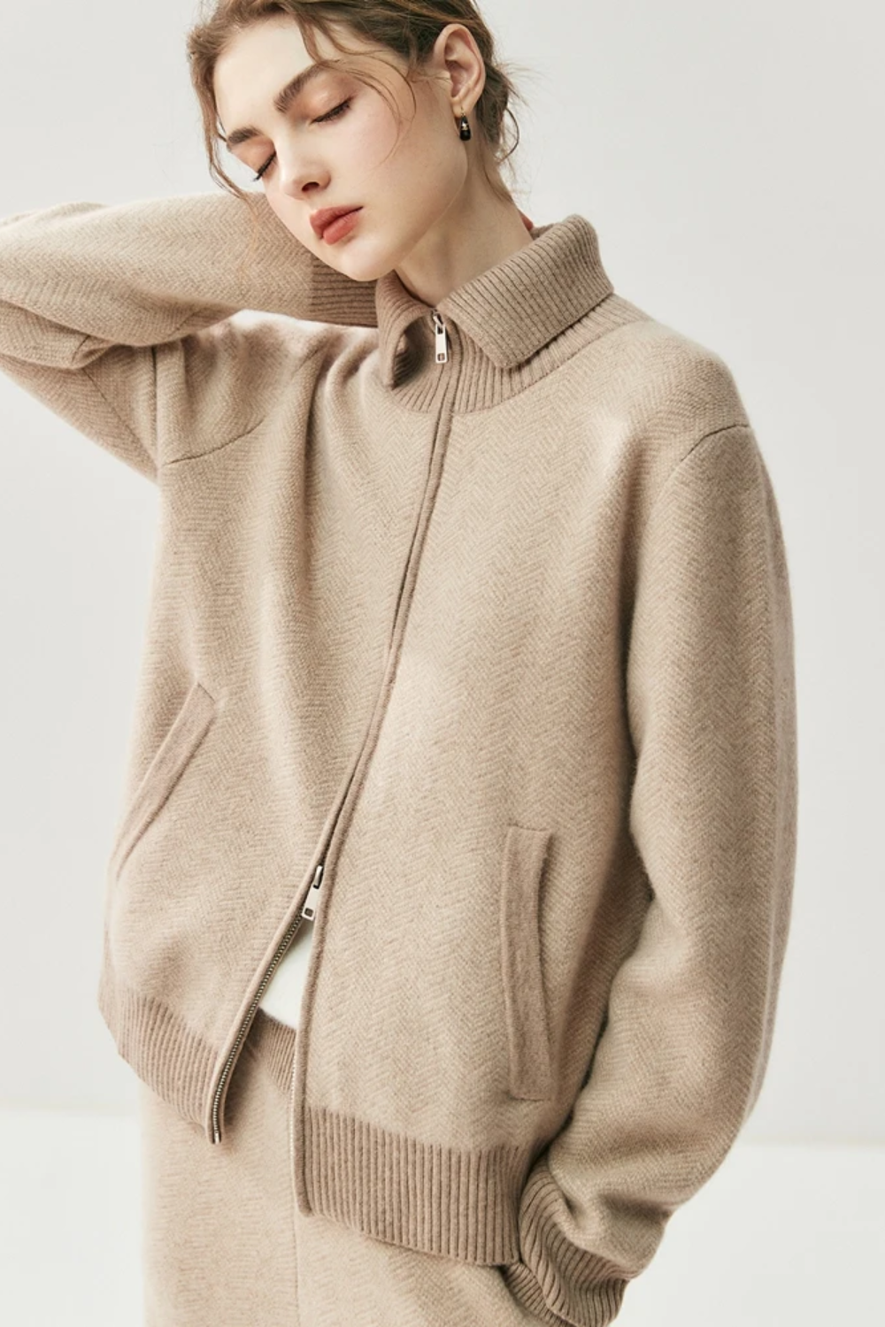 Close-up of a person wearing a camel zip-up sweater against a light background