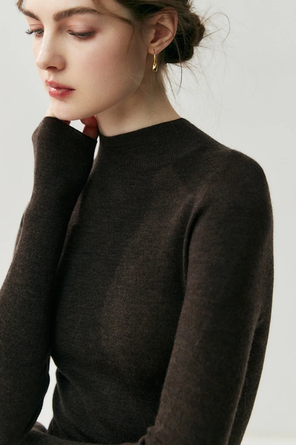 Woman wearing a dark brown sweater against a plain background